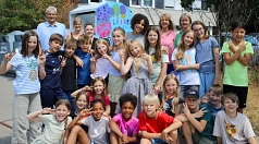 In dem Bild sieht man einige Kinder, die vor einem bemalten Altkleider-Container stehen.
