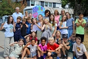 In dem Bild sieht man einige Kinder, die vor einem bemalten Altkleider-Container stehen.