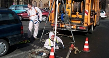 Das Bild zeigt einen Mitarbeiter des DBM, der bereits bis zur Körpermitte in einen Schacht hinabgestiegen ist. Er ist durch ein Seil gesichert und trägt einen Ganzkörperanzug.