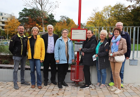 Eine Gruppe von Personen steht mit der Stadträtin um den neuen Aschenbecher an der Bushaltestelle.