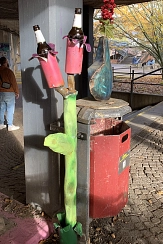 Das Foto zeigt einen Abfalleimer neben dem eine geschmiedete und bunt lackierte Blume mit zwei Blüten hochragt. In die Blüten kann jeweils eine Flasche gestellt werden.&nbsp;&copy;&nbsp;DBM, Sonja Stender