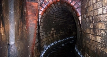 Das Bild zeigt ein gemauertes Eiprofil mit einer Höhe von 1,70 m. Bei sehr starken Regen können selbst solche großen Leitungen komplett mit Wasser gefüllt sein. Im Vordergrund kann man die Sandstein-Rutsche erkennen, mit deren Hilfe das Wasser vom Parkhau