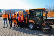 Fünf Menschen stehen vor der neuen elektrischen Kehrmaschine. Sie blicken in die Kamera und tragen orangene Warnwesten.