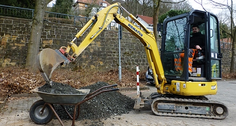Das Foto zeigt einen Mitarbeiter des DBM beim Beladen einer Schubkarre mit einem kleinen Bagger.