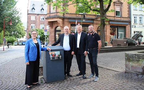 Vier Personen stehen um den Abfalleimer mit den Pfandringen.