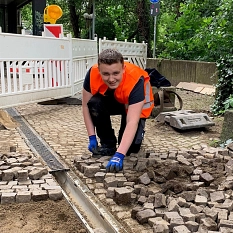 Auf dem Foto sieht man einen jungen Mann in Warnkleidung auf einer Baustelle, der Kopfsteinpflaster bereit legt.&nbsp;&copy;&nbsp;DBM, Sonja Stender