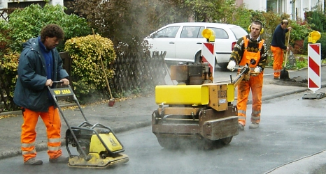 Das Foto zeigt zwei Mitarbeiter des DBM die mit Rüttelplatten eine neue Asphaltdecke verdichten.