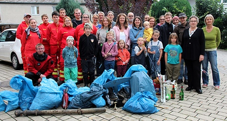 Eine Gruppe von Menschen, Kinder und Erwachsene,  steht hinter blauen, mit Müll gefüllten Säcken.