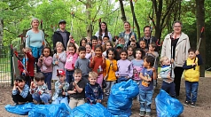 Eine Gruppe von Kindern stehen aufgestellt mit Müllzangen in der Hand in einem Wäldchen. Vor Ihnen liegen gefüllte blaue Säcke. Einige Erwachsene stehen in der hinteren Reihe.