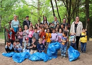 Eine Gruppe von Kindern stehen aufgestellt mit Müllzangen in der Hand in einem Wäldchen. Vor Ihnen liegen gefüllte blaue Säcke. Einige Erwachsene stehen in der hinteren Reihe.
