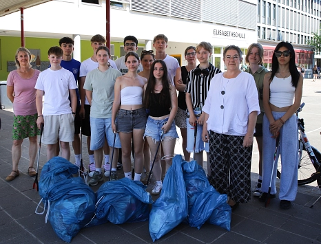 Eine Gruppe von Menschen steht vor einem Gebäude. Einige von Ihnen halten Greifzangen in der Hand. Vor ihnen liegen gefüllte blaue Säcke.
