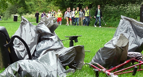 Das Foto zeigt Abfallsäcke und einen Fahrradrahmen ohne Reifen im Vordergrund. Dahinter gehen Kinder in Warnwesten mit Papierzangen und sammeln Abfälle ein.&nbsp;&copy;&nbsp;DBM, Sonja Stender